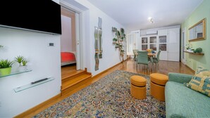 A modern living room with a sofa, ottomans, a patterned rug, and a dining area with chairs and a table. - GuestHost - Mercatovecchio Ivy House (Udine)