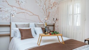 A bedroom with a bed, a bedside table with a bottle and glasses, and a floral wall mural. - GuestHost - Mercatovecchio Ivy House (Udine)