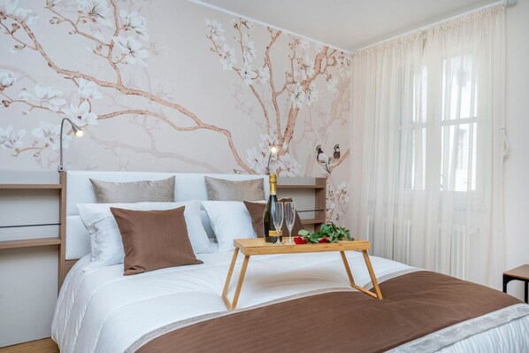 Un dormitorio con una cama, una mesita de noche con una botella y vasos, y un mural floral en la pared.