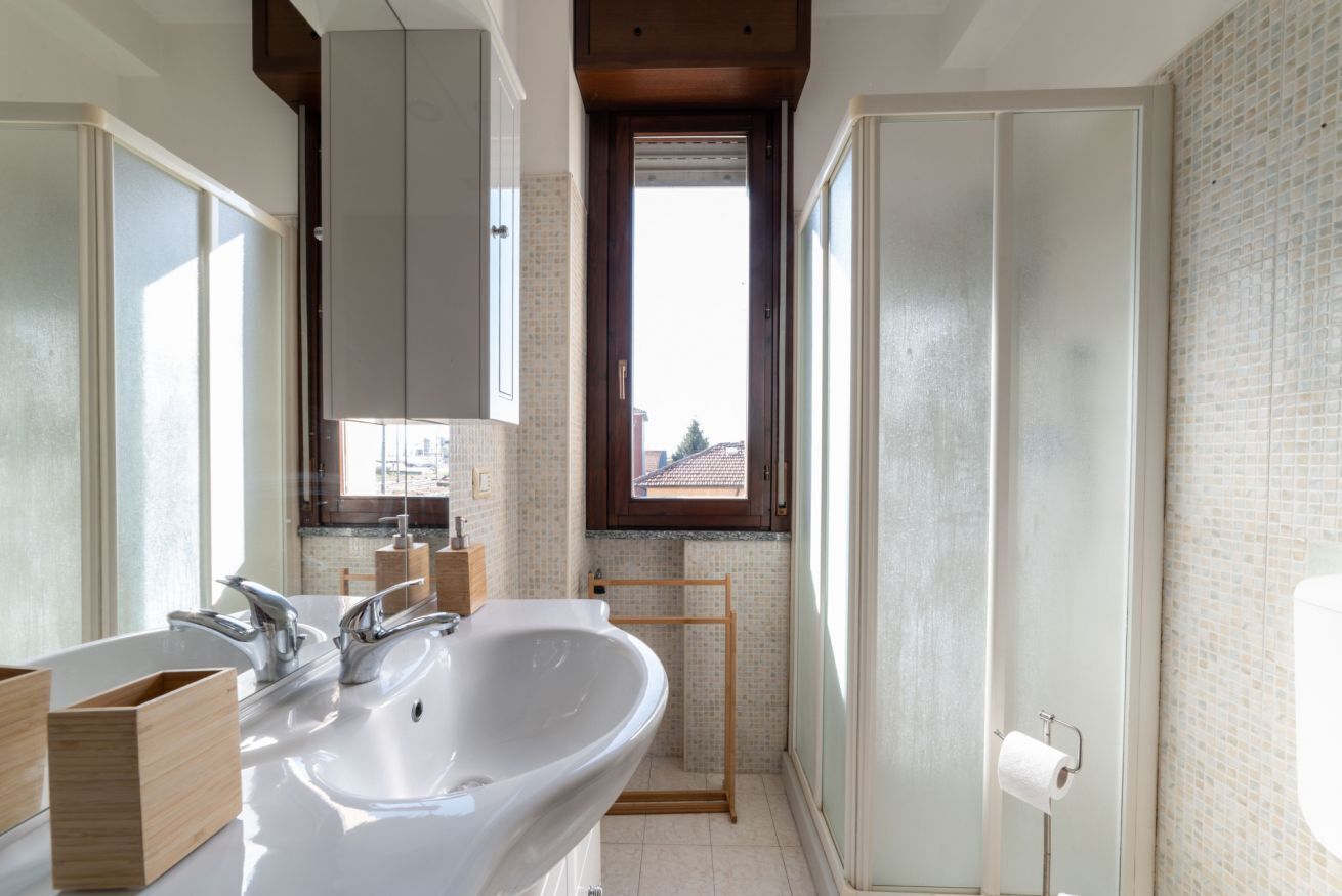 A bathroom with a large sink, wooden cabinets, a window, and a toilet paper holder.