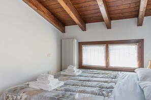 A bedroom with a wooden ceiling, a radiator, a window with blinds, and a bed with folded towels.