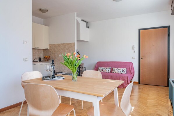 A modern kitchen with white cabinets, a wooden dining table with chairs, and a pink sofa in the living area.