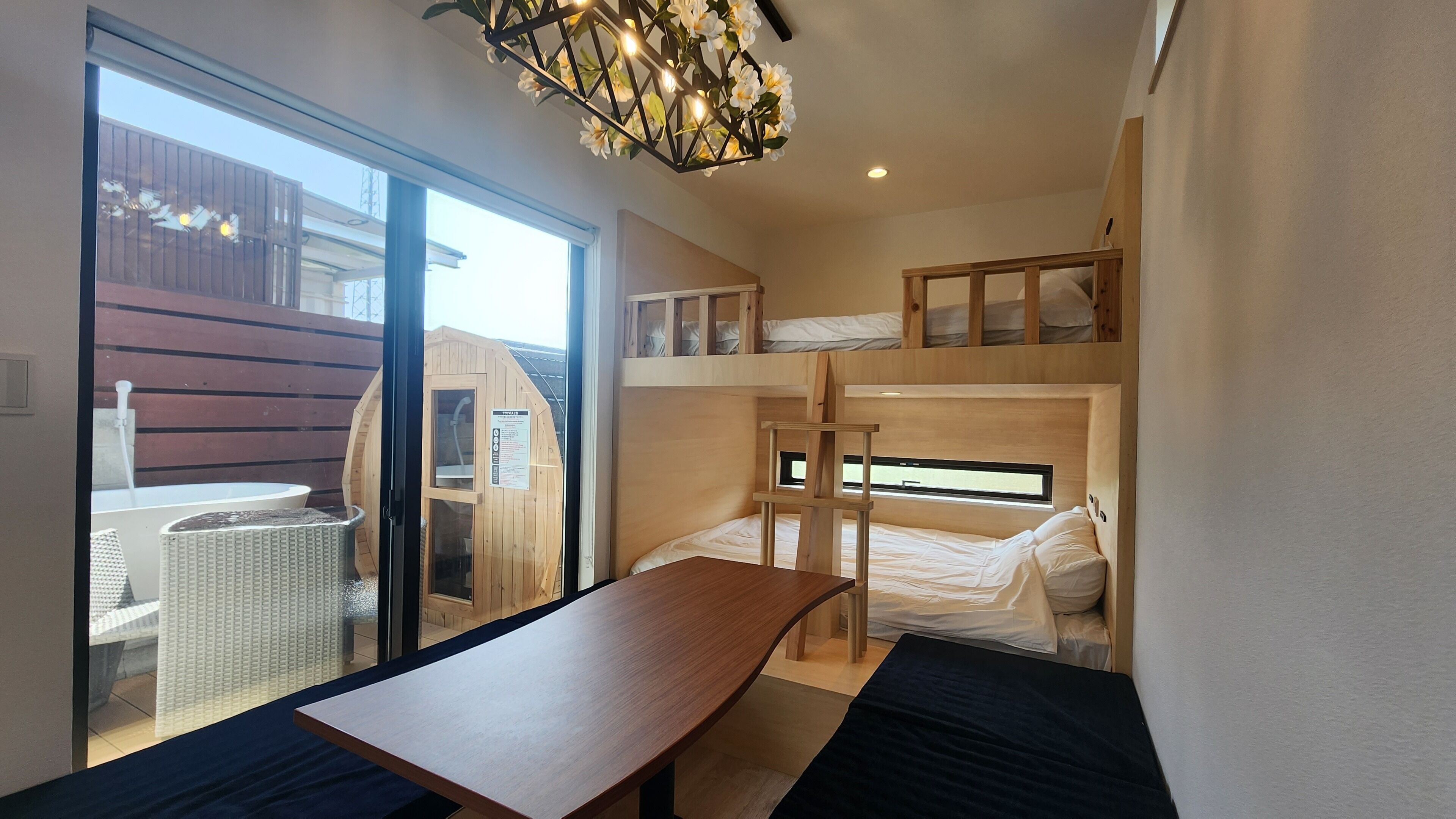 A bunk bed room with a wooden table and a bench, a sauna, and a view of the outside.