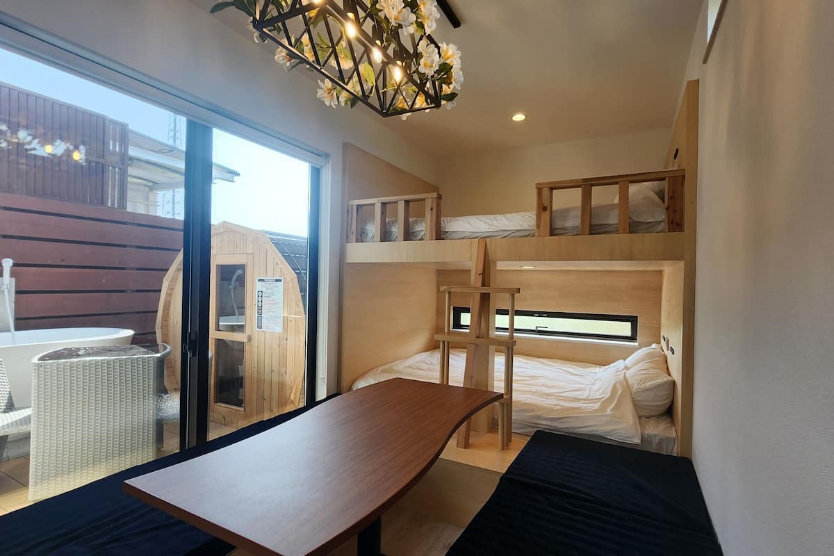 A bunk bed room with a wooden table and a bench, a sauna, and a view of the outside.