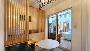 A room with a wooden partition, a round table, and a view through a glass door to an outdoor area with a white structure. - ZUMI TERRACE UCHINAAMIYA RESORT (Miyakojima)