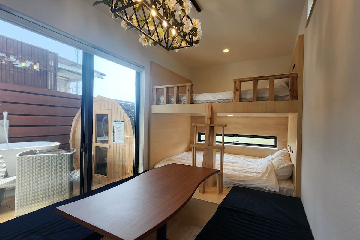 A bunk bed room with a wooden table and a bench, a sauna, and a view of the outside.