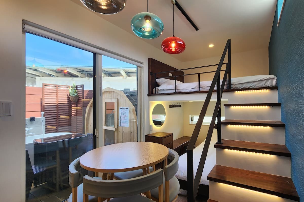 A compact room with a bunk bed, a small table, and a staircase with built-in lighting.