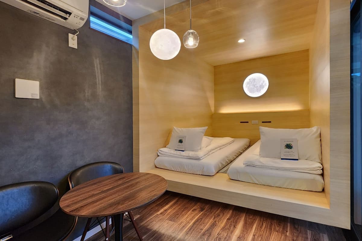 A modern hotel room with a wooden wall, two beds with white bedding, a round wooden table, and two pendant lights.