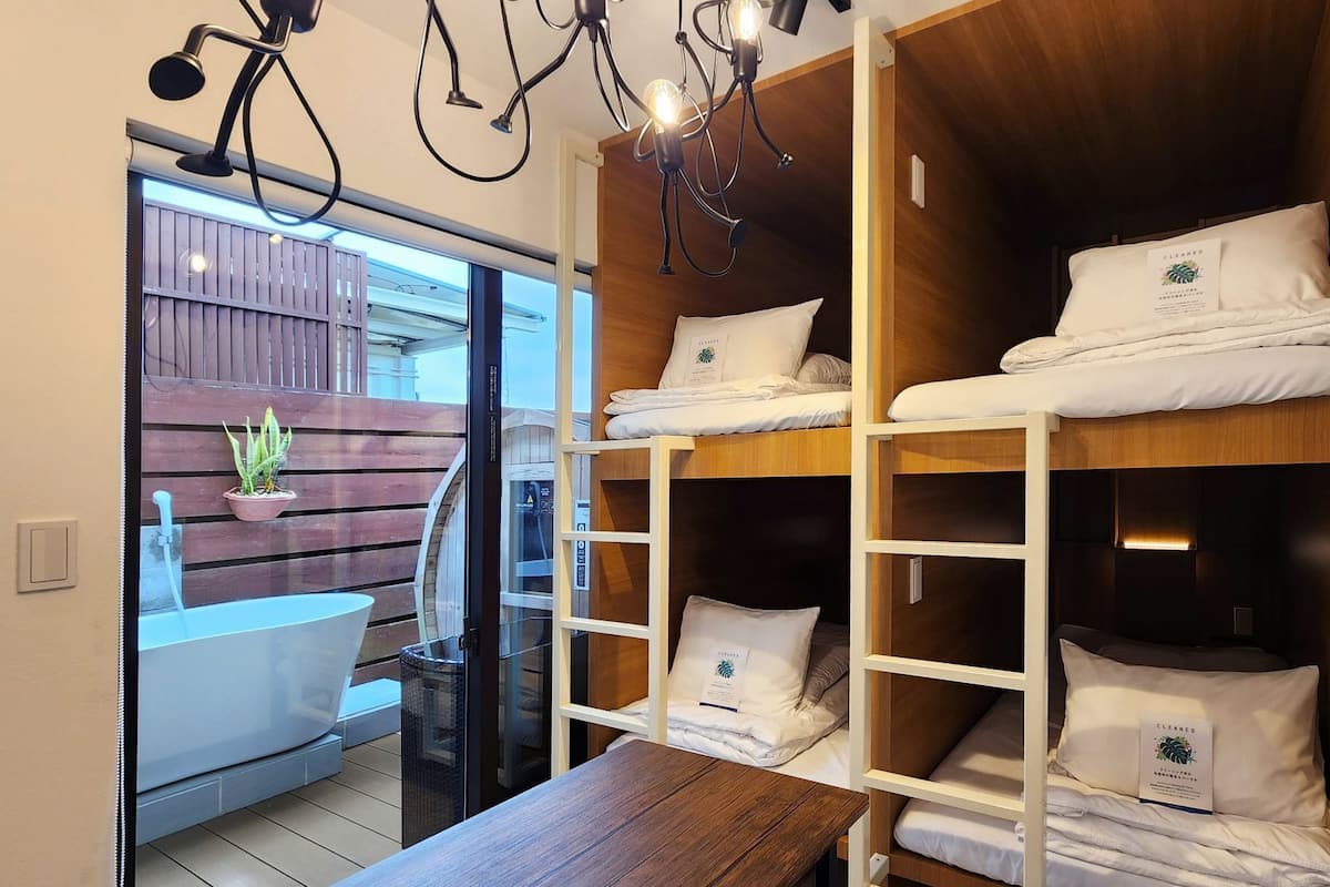 A hotel room with bunk beds, a wooden table, and a small balcony with a potted plant.