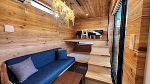 A cozy cabin interior with a wooden wall, a blue sofa, a small table, and a staircase leading to a loft area. - ZUMI TERRACE UCHINAAMIYA RESORT (Miyakojima)