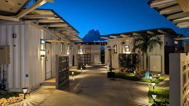 A corridor with multiple doors, each marked with a number. There are outdoor lights and a palm tree. - ZUMI TERRACE UCHINAAMIYA RESORT (Miyakojima)