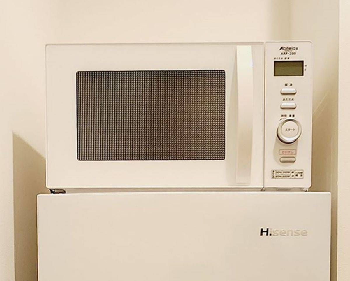 Un horno microondas Hisense con pantalla digital y botones de control sobre un refrigerador blanco.