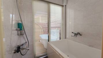 A bathroom with a bathtub, a shower with a handheld showerhead, and a window with blinds.