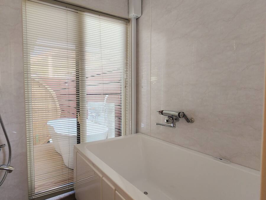 A bathroom with a bathtub, a shower with a handheld showerhead, and a window with blinds.