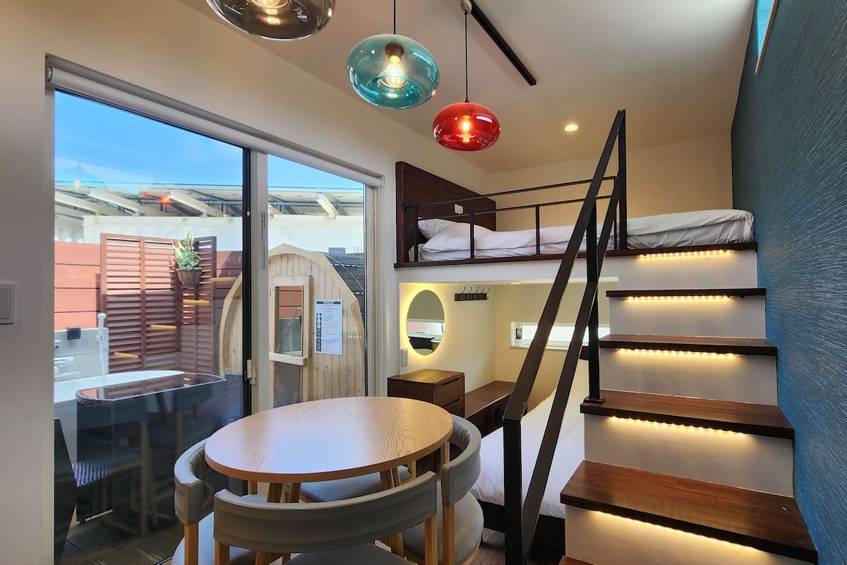 A compact room with a bunk bed, a small table, and a staircase with built-in lighting.