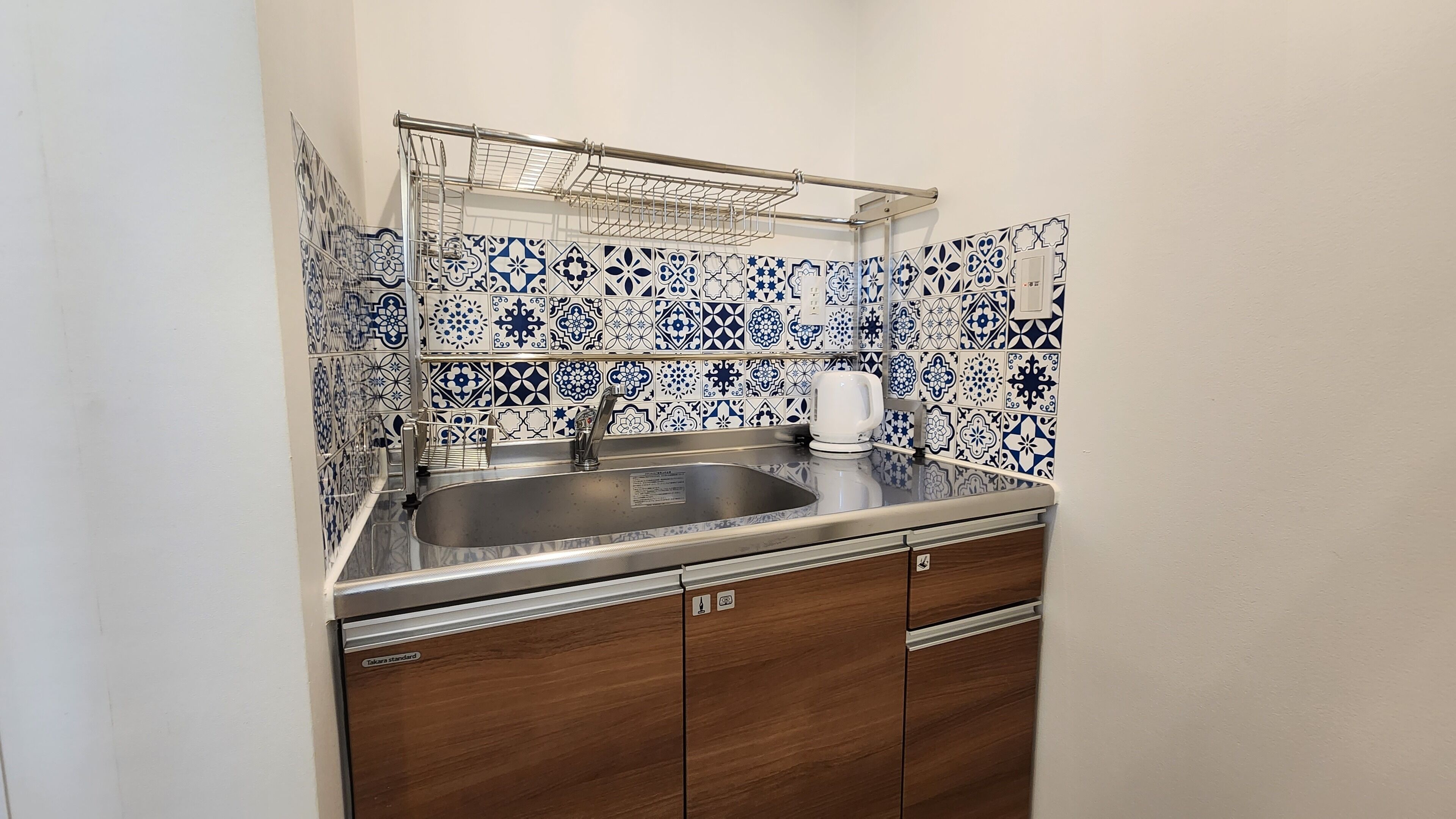 A compact kitchen with a sink, a kettle, and a metal drying rack.