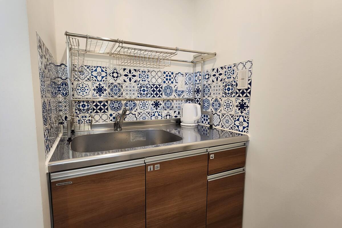 A compact kitchen with a sink, a kettle, and a metal drying rack.
