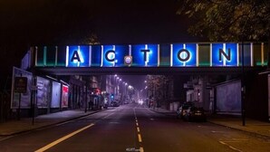 A street under a brightly lit sign with the word "ACTON" in large letters.