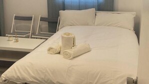 A hotel room with a bed, two chairs, a small table, and a window with curtains.