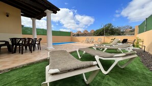 Ein Poolbereich mit Liegestühlen und einem Tisch, einer Pergola und Blick auf einen Swimmingpool sowie entfernte Gebäude.