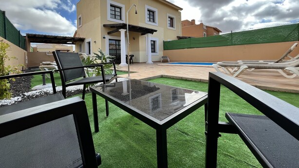 Ein Haus mit Schwimmbad, Terrasse und Gartenmöbeln sowie einem gepflegten Rasen.