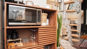 Una zona de cocina con microondas, repisas de madera, cafetera y una planta colgante.