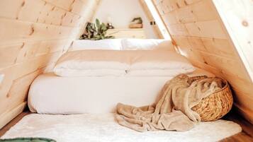A cozy attic bedroom with a wooden sloped ceiling, a bed with white bedding, a woven basket, and a white rug.