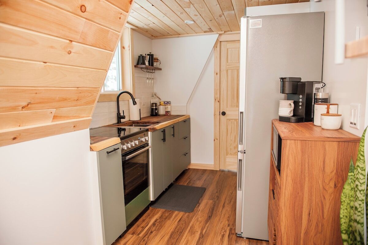 Une cuisine compacte dotée de meubles en bois, d’un four encastré, d’un réfrigérateur et d’une machine à café.