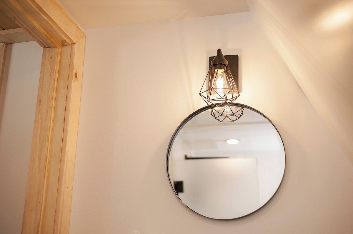A round mirror with a light fixture above it, mounted on a white wall.
