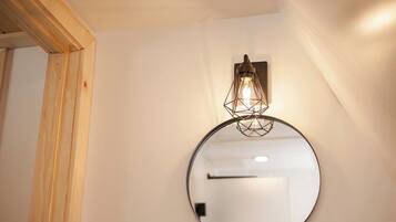 A round mirror with a light fixture above it, mounted on a white wall.