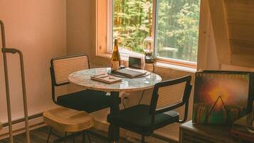 A small, cozy room with a round table, two chairs, a bottle of wine, a small lamp, and a painting on the wall.