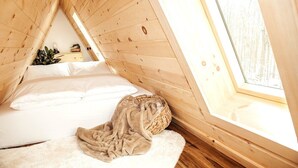 Un dormitorio acogedor en el ático con techo inclinado, un ventanal grande y una cama cómoda con manta.