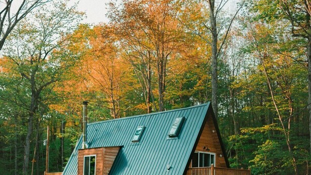 Una cabaña con techo inclinado, fachada de madera y una terraza con mobiliario exterior.