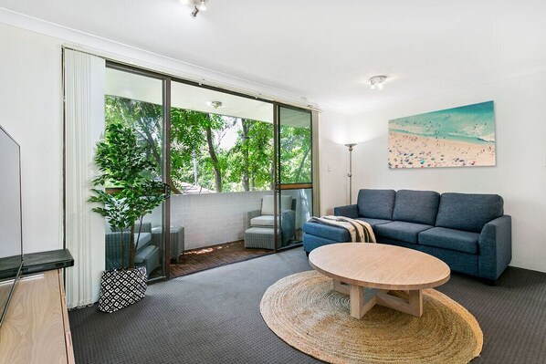 A modern living room with a blue sofa, a round coffee table, and a painting of a beach scene. - Bondi Bliss Lamrock - 1 minute to beach + Parking (Bondi Beach)