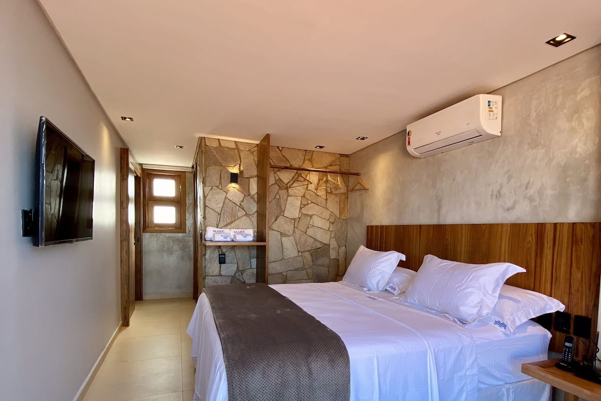 A modern bedroom with a large bed, a TV, a stone wall, and a wooden headboard.