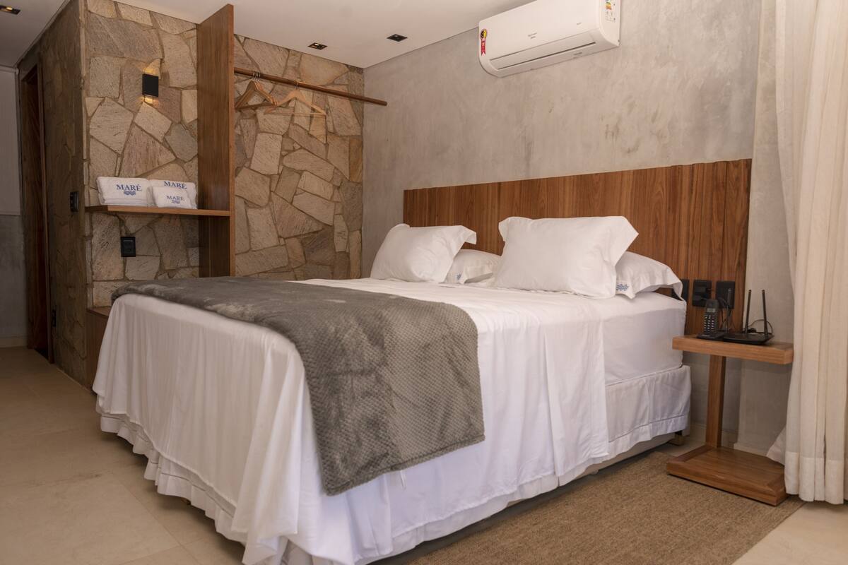 A bedroom with a stone wall, a wooden headboard, a bed with white bedding, a bedside table, and a hanging rack.
