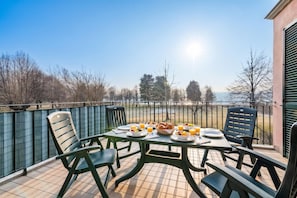 A balcony with a table set for breakfast, chairs, and a view of the landscape. - Porto Letizia Ortensia 5, Porlezza, Italy (Porlezza)