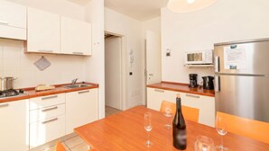 A modern kitchen with white cabinets, a wooden countertop, a stainless steel refrigerator, and a dining table with chairs.