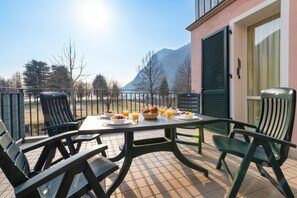 A terrace with a table set for breakfast, chairs, and a view of mountains. - Porto Letizia Ortensia 5, Porlezza, Italy (Porlezza)