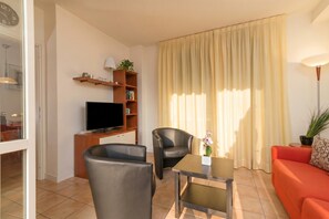 A living room with a TV, two chairs, a sofa, a table, a bookshelf, and a window with curtains. - Porto Letizia Ortensia 5, Porlezza, Italy (Porlezza)