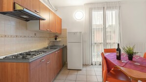 A kitchen with wooden cabinets, a gas stove, a white refrigerator, and a dining table with chairs. - Porto Letizia Mozart 5, Porlezza, Italy (Porlezza)