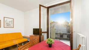A room with a red table, a yellow sofa, a TV, and a balcony with a view. - Porto Letizia Mozart 4, Porlezza, Italy (Porlezza)