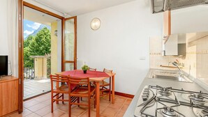 A compact kitchen with a gas stove, a dining table with chairs, a TV on a cabinet, and a sliding glass door leading to an outdoor area. - Porto Letizia Mozart 4, Porlezza, Italy (Porlezza)