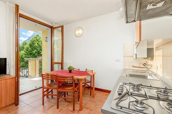 A compact kitchen with a gas stove, a dining table with chairs, a TV on a cabinet, and a sliding glass door leading to an outdoor area. - Porto Letizia Mozart 4, Porlezza, Italy (Porlezza)