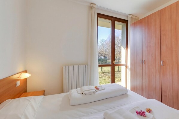 A hotel room with a bed, a window with curtains, a radiator, and a wardrobe. - Porto Letizia Verdi 1, Porlezza, Italy (Porlezza)