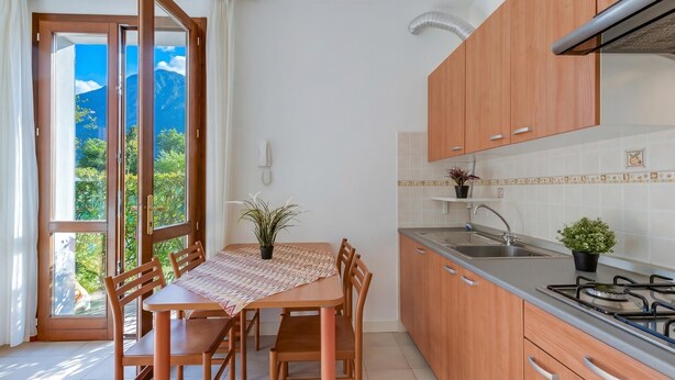 A kitchen with wooden cabinets, a gas stove, a sink, and a dining table with chairs. - Porto Letizia Verdi 1, Porlezza, Italy (Porlezza)