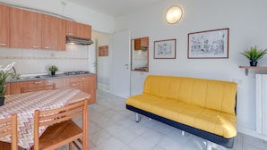 A compact kitchen with wooden cabinets, a dining table with a patterned tablecloth, and a yellow sofa. - Porto Letizia Verdi 1, Porlezza, Italy (Porlezza)