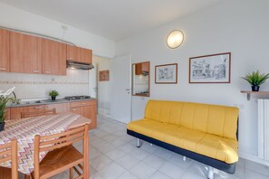 A compact kitchen with wooden cabinets, a dining table with a patterned tablecloth, and a yellow sofa. - Porto Letizia Verdi 1, Porlezza, Italy (Porlezza)