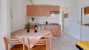 A modern kitchen with wooden cabinets, a dining table with chairs, a small plant, and a wine bottle. - Porto Letizia Verdi 1, Porlezza, Italy (Porlezza)