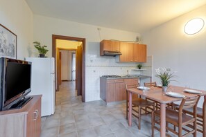 A kitchen with wooden cabinets, a dining table with chairs, a TV, and a potted plant. - Porto Letizia Puccini 3, Porlezza, Italy (Porlezza)